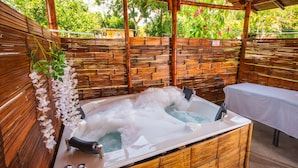 Un jacuzzi en un área exterior cubierta, con un cerramiento de madera y una mesa cerca.