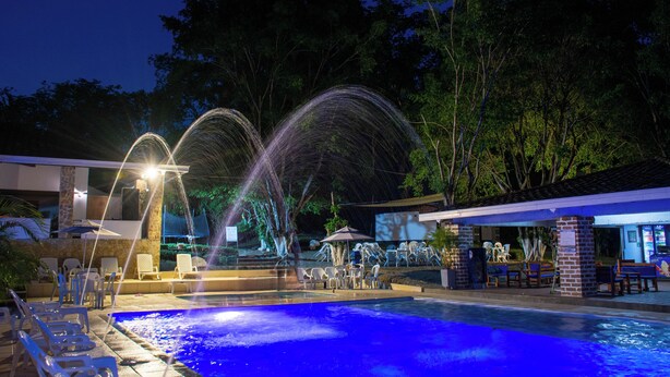 Un área de piscina con una fuente, sillas de descanso y una zona de estar cubierta.