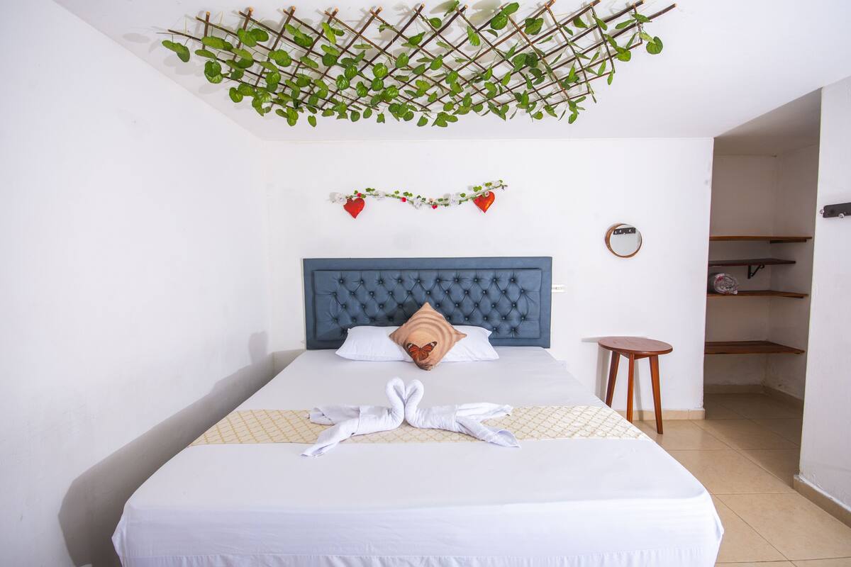 Una cama bien hecha con un cabecero azul, un cojín con forma de corazón y una toalla dispuesta con arte sobre la cama.