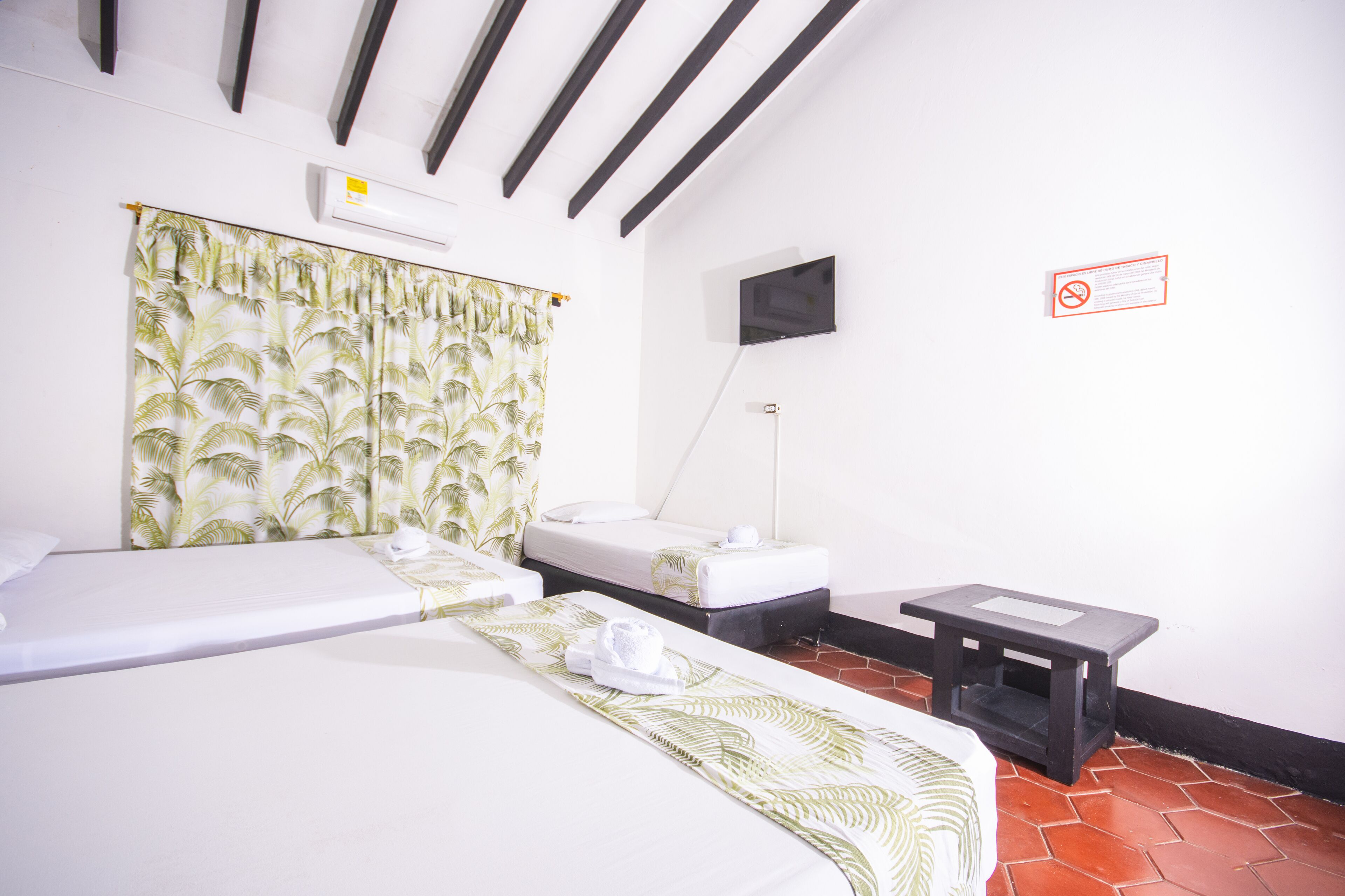 Habitación de hotel con una cama, una mesita de noche, un televisor y una ventana con cortinas.