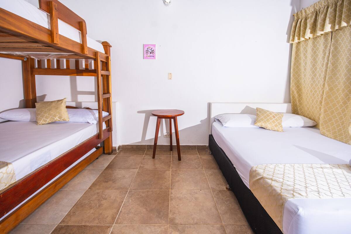 Una habitación con dos camas, una con cabecera de madera y la otra con estructura negra. En el centro hay una mesita.