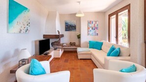 Ein Wohnzimmer mit weißen Sofas, einem Fernseher und Kunstwerken an den Wänden.