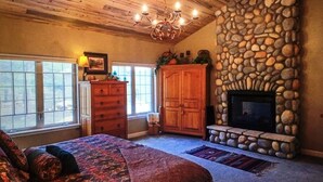 Een slaapkamer met een stenen openhaard, houten plafond en een groot bed.