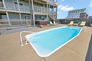 Une piscine équipée d’un escalier en métal, entourée d’une terrasse avec des chaises longues et un jacuzzi.