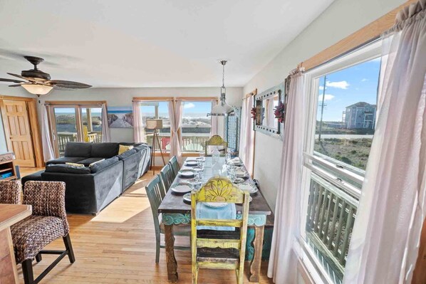 A spacious living area with a dining table set for four, a sofa, and a view of the ocean through large windows.
