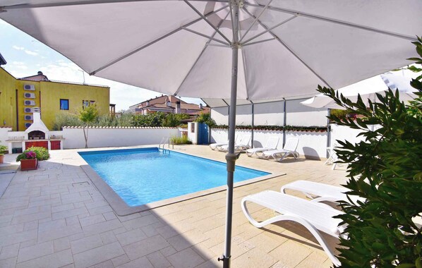 Une piscine avec un parasol blanc, des chaises longues et un espace barbecue.
