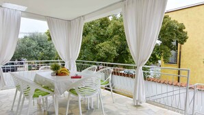 Un balcone con tavolo e sedie, sullo sfondo un edificio giallo e una ringhiera bianca.