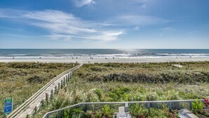 A beach view with a wooden boardwalk leading to the shore, a signboard, and a railing in the foreground. - Spacious and newly updated 2nd floor walk-up + Free Attraction Tickets! (North Myrtle Beach)
