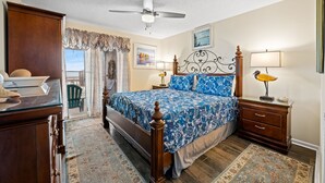 A bedroom with a bed, wooden nightstands, a desk, a chair, a ceiling fan, and a view through a door. - Spacious and newly updated 2nd floor walk-up + Free Attraction Tickets! (North Myrtle Beach)