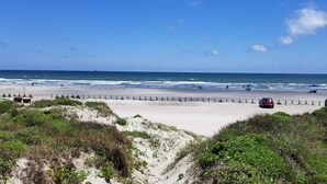 Une plage avec un rivage sablonneux, une clôture en bois et deux voitures garées sur la plage.