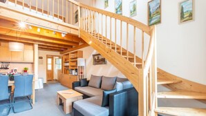 A spacious living area with a wooden staircase, a sofa, a dining table, and a kitchen in the background. - Am Hohen Bogen by Interhome (Arrach)