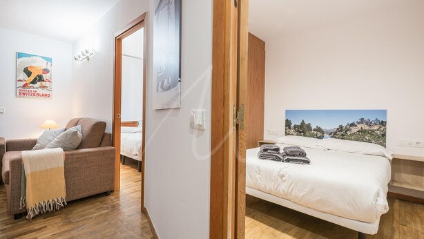A bedroom with a bed, a sofa, and a wooden floor. - Bonaigua 006 (Baqueira)