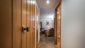 A hallway with wooden doors leading to a living area with a sofa and a poster on the wall. - Bonaigua 006 (Baqueira)