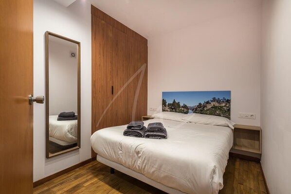 A bedroom with a bed, a wooden wardrobe, a large mirror, and a painting of a landscape.