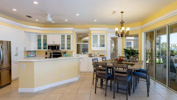 A modern kitchen with a central island, white cabinets, and a dining area with chairs. - Magic Sunset - Luxurious Vacation Home with Gulf (Cape Coral)