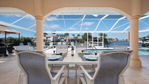 Ein Essbereich im Freien mit Tisch für zwei Personen, mit Blick auf einen Pool und eine Marina.