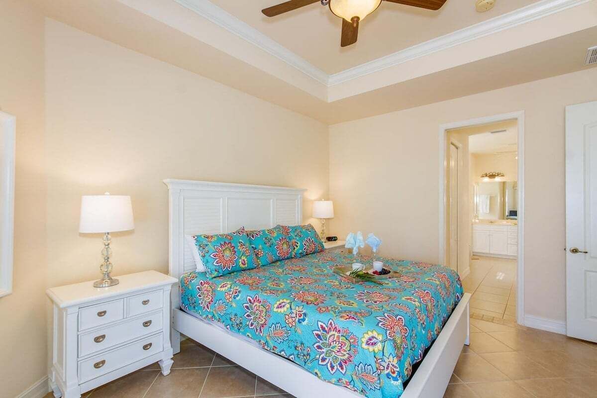 A bedroom with a bed, nightstands, a ceiling fan, and a door leading to another room.