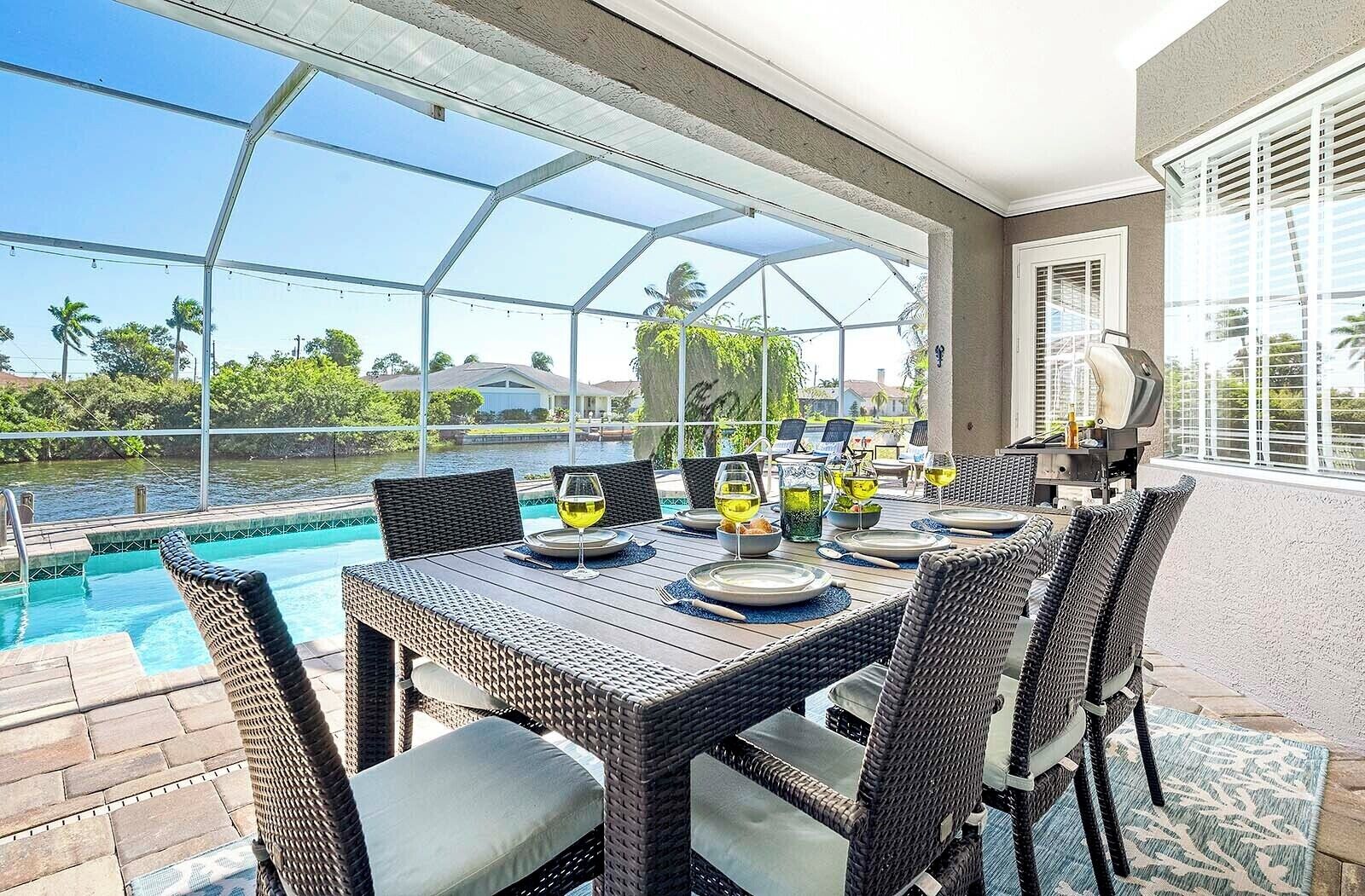 Un área de comedor al aire libre con vista a la piscina, mobiliario de mimbre y un recinto de cristal.