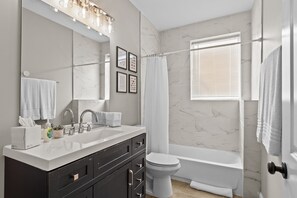 A modern bathroom with a large mirror, a white sink, dark cabinets, a toilet, and a bathtub.