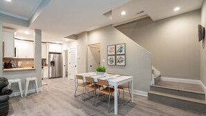 A modern kitchen with white cabinets, a stainless steel refrigerator, and a dining area with a white table and chairs. - Historic 3BR Near Barnes Jewish Hospital | Walkable CWE | Dog-Friendly (St Louis)