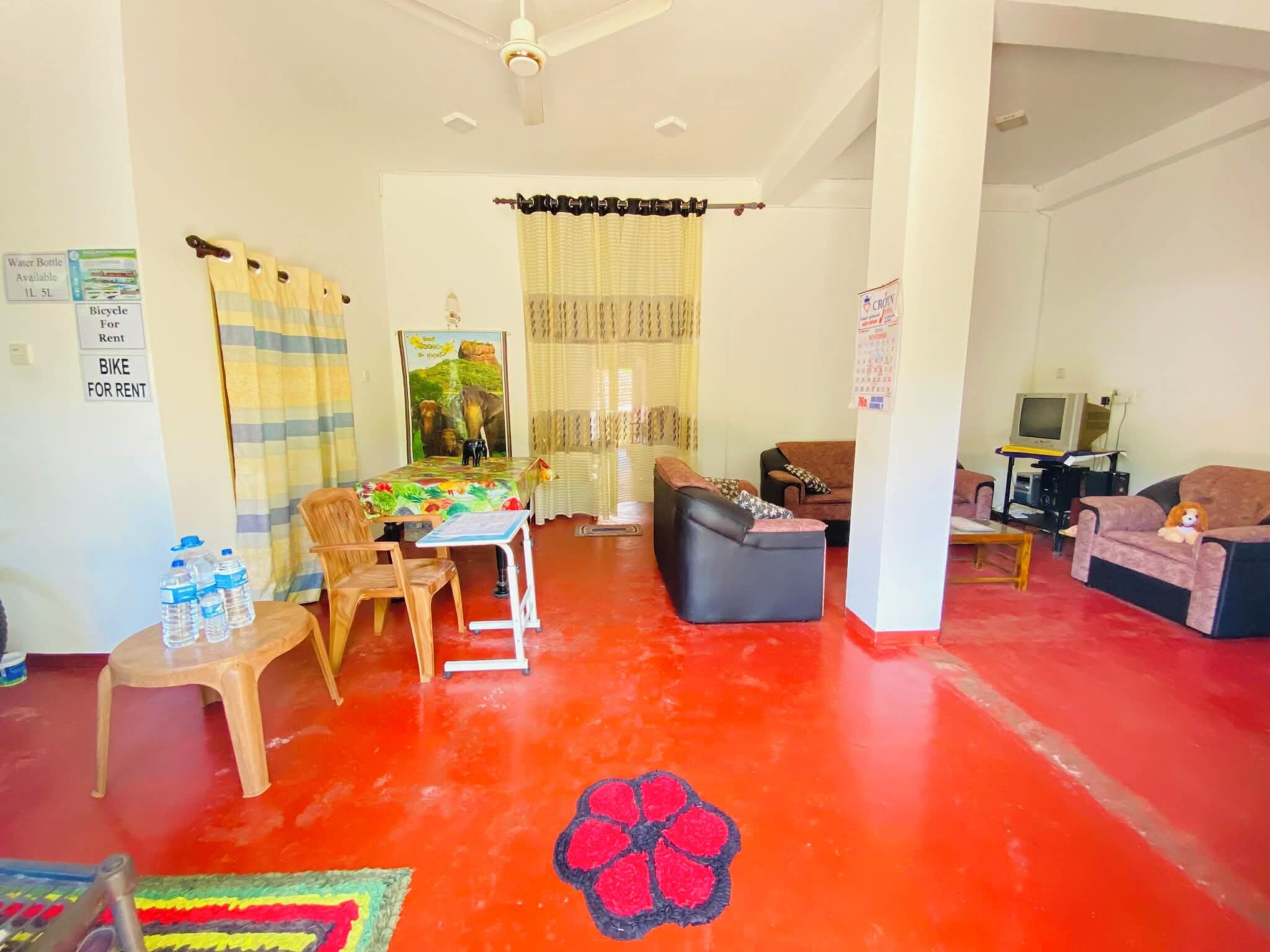 Una sala de estar con piso rojo, una mesa con sillas, un sofá, un televisor y un peluche.