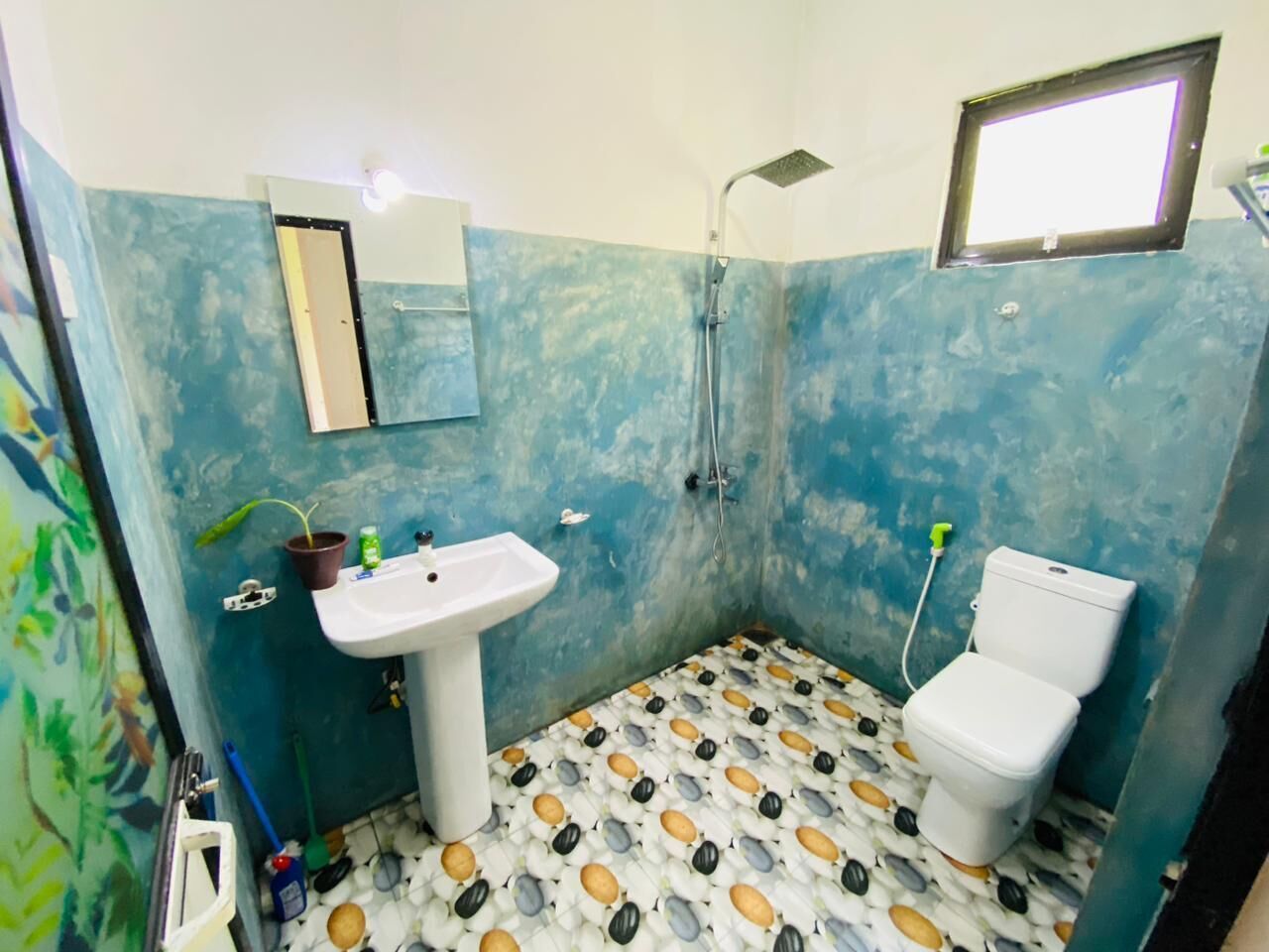 A bathroom with a sink, toilet, and shower. The walls are painted blue, and the floor has a patterned tile design.