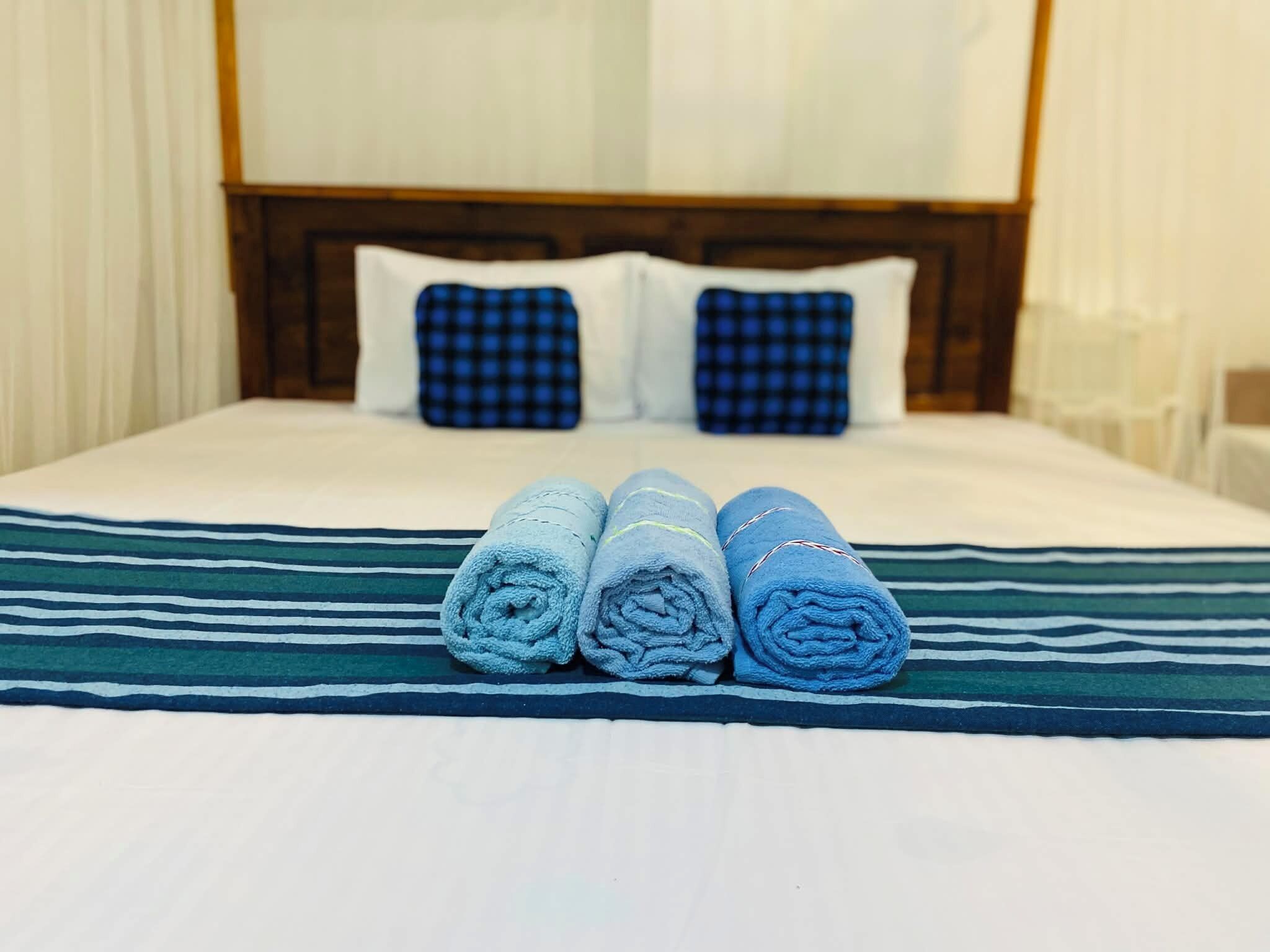 A hotel room with a neatly made bed, striped bedspread, and two checkered pillows.