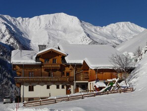 En træchalet med balkon, omgivet af sneklædte bjerge.