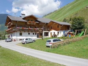 A two-story wooden house with a balcony, a car parked in front, and a playground with a slide.