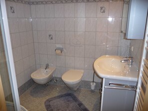 Et badeværelse med bidét, toilet, vask og et håndklædetørrestativ.