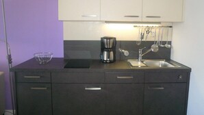 A modern kitchen with a dark countertop, a coffee maker, a sink, and hanging utensils. - App. Meinecke 29 O, Germany (Sylt)