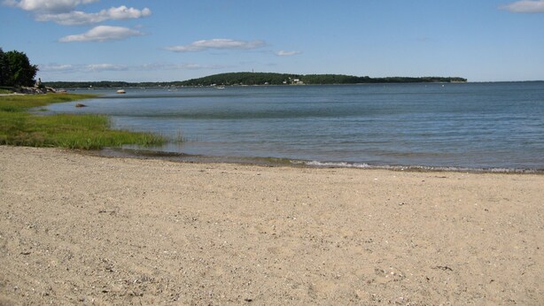A beach with a sandy shore, calm water, and a distant island with buildings.