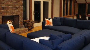 A living room with a brick fireplace, a large blue sectional sofa, and a dining area with a table and chairs.