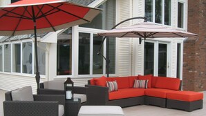 A patio with a sectional sofa, two armchairs, a table, and a red umbrella.
