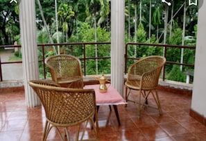 A balcony with wicker chairs and a table, overlooking a lush green landscape.
