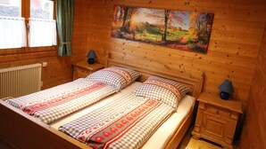 Een slaapkamer in een houten chalet met twee bedden, een landschapsschilderij en een raam met gordijnen.