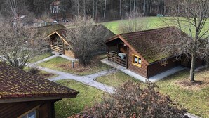 Een blokhut met schuin dak en een veranda, omringd door gras en bomen.