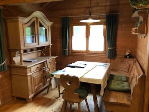 Ein Holzblockhaus-Interieur mit Esstisch, Stühlen, einem Schrank und einer Bank.