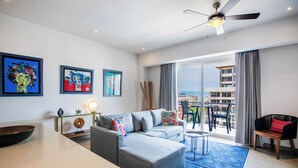 A modern living room with a grey sofa, a dining table, and a balcony with a view. - Top floor 1BR | 2 Pools & Gym | Romantic Zone (Puerto Vallarta)