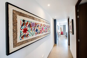 A hallway with a large abstract painting on the wall, a wooden door, and a tiled floor.