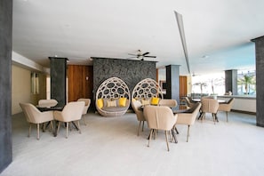 En moderne hotellobby med et siddeområde med runde, vævede stole med hynder, en ventilator i loftet og en væg med geometrisk mønster.
