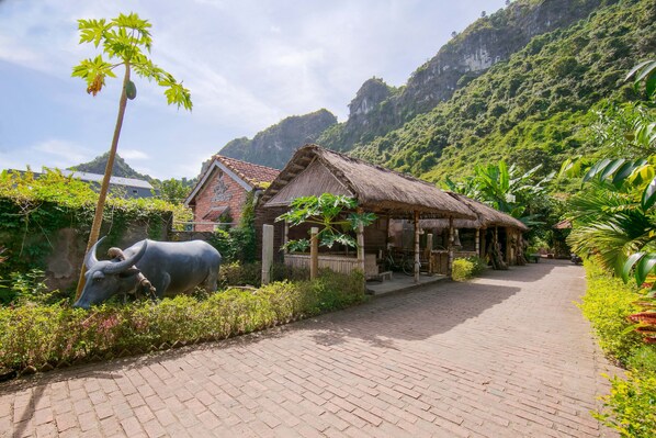 A rustic building with a thatched roof, surrounded by lush greenery and a brick pathway. - Lan Homestay (Hai Phong)