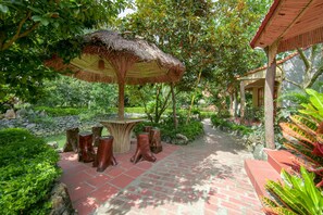A garden pathway with a thatched umbrella, wooden stumps, and lush greenery. - Lan Homestay (Hai Phong)