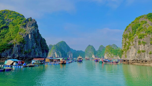 A coastal scene with boats docked along the shore, surrounded by lush green cliffs. - Lan Homestay (Hai Phong)