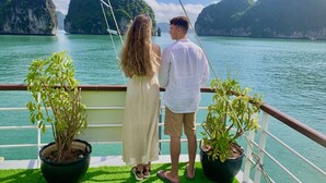 A couple standing on a boat deck with potted plants, overlooking a calm lake with mountains in the background. - Lan Homestay (Hai Phong)