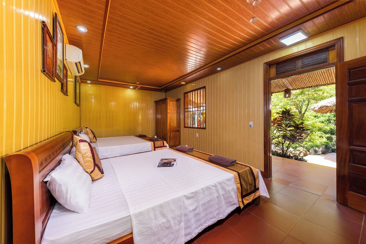A hotel room with two beds, wooden ceiling, and a view of greenery outside.