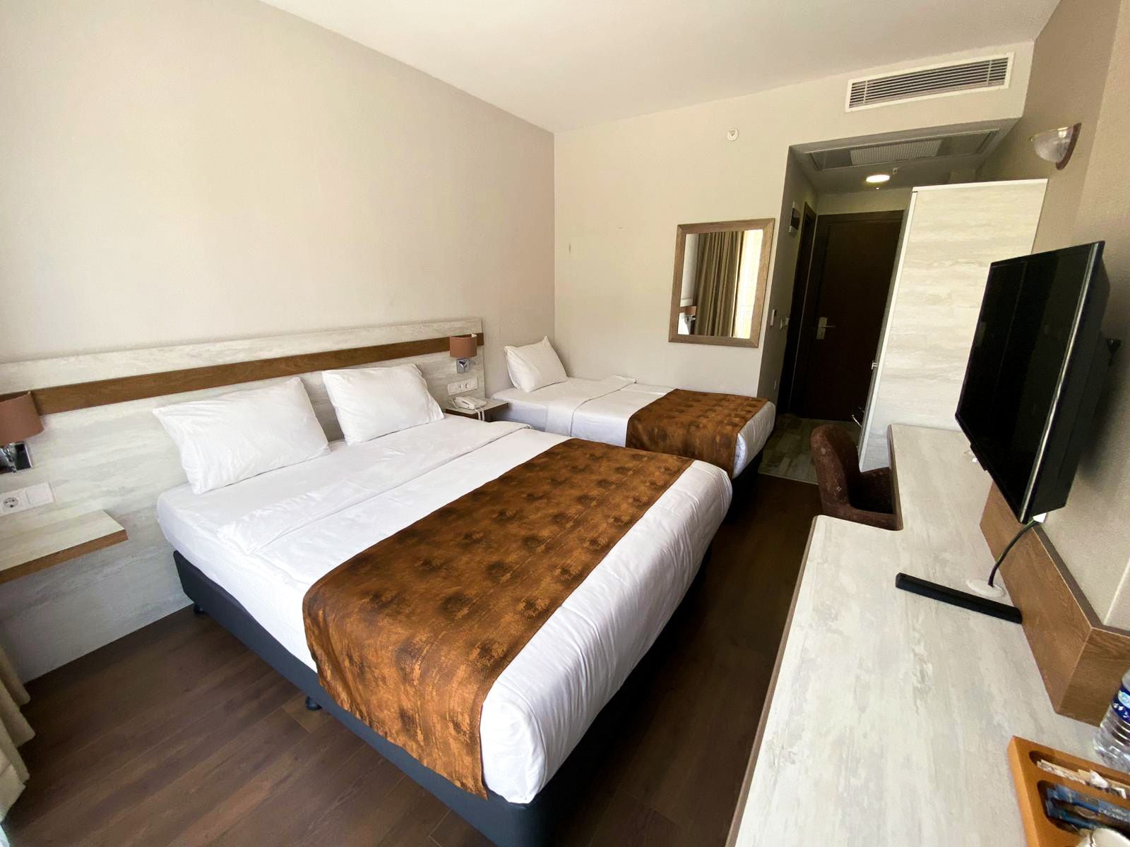 Hotellihuone, jossa on kaksi sänkyä, televisio, työpöytä ja peili.