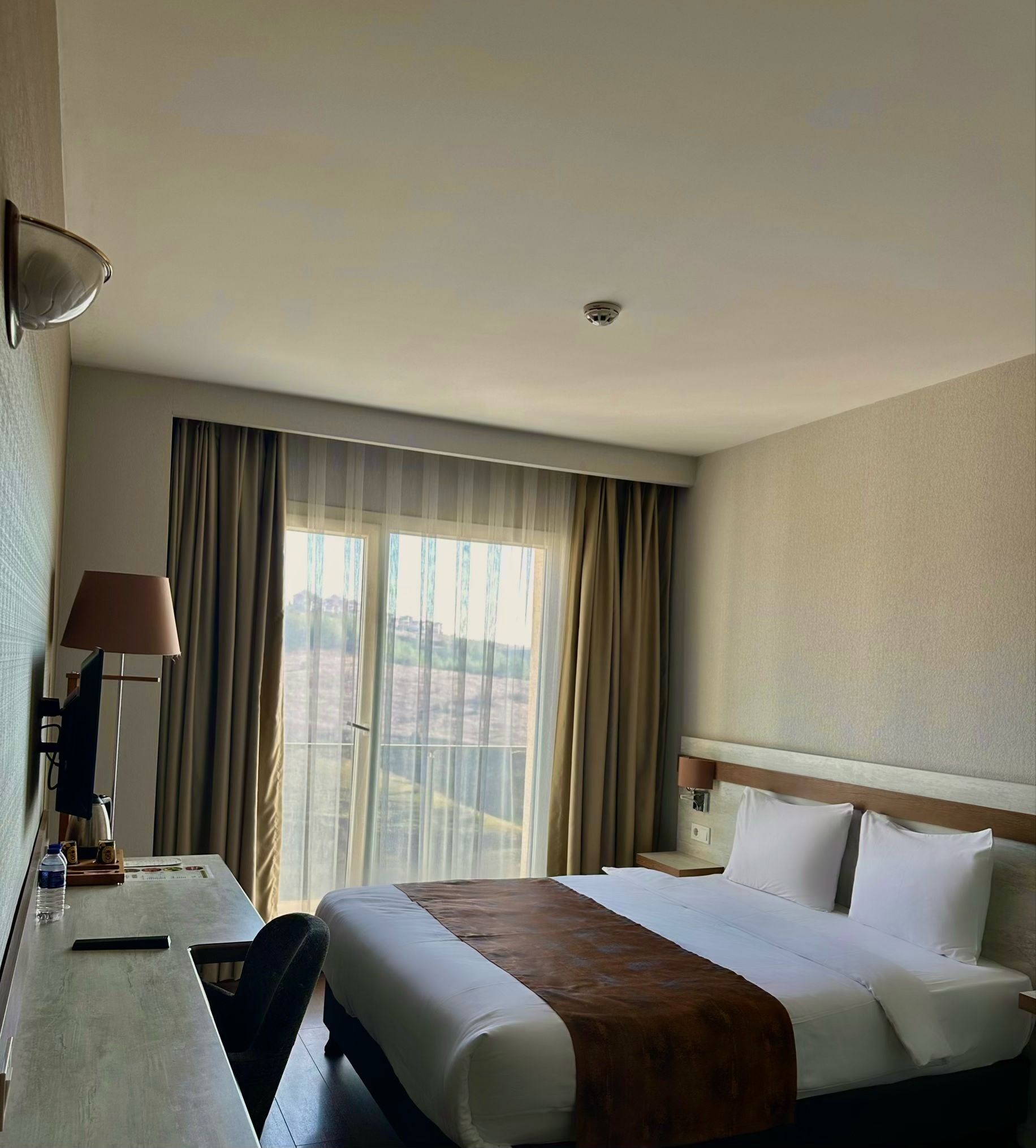 A hotel room with a bed, a desk, a lamp, and a window with curtains.
