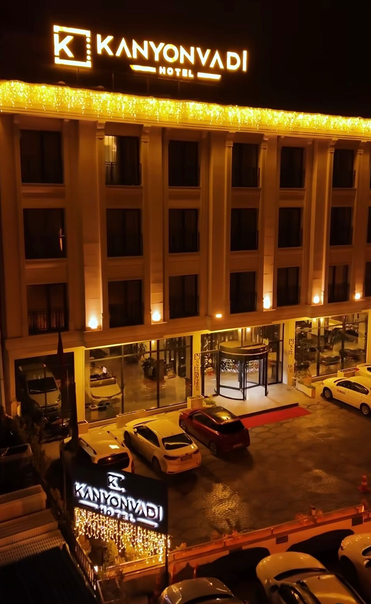 A hotel with a prominent sign, multiple floors, and a parking area with several cars.