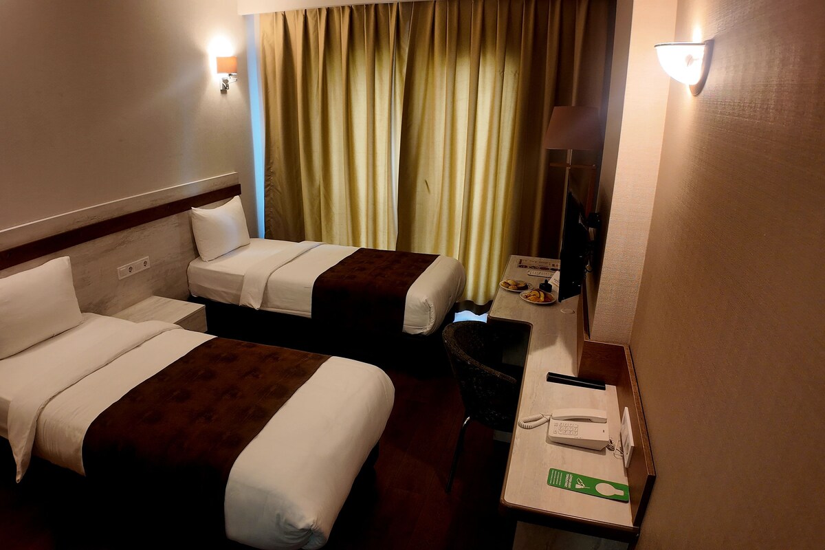 A hotel room with two beds, a desk with a telephone, and a mirror.